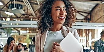 woman walking through office space holding laptop